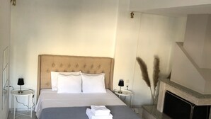 A modern bedroom with a large bed, bedside tables, a fireplace, and a small round table. - Greece Apartments Now (Patra Achaia)
