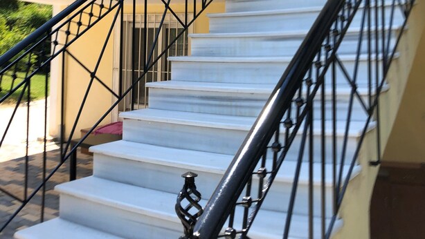 A staircase with a black metal railing leading to a landing with a window and a door. - Greece Apartments Now (Patra Achaia)