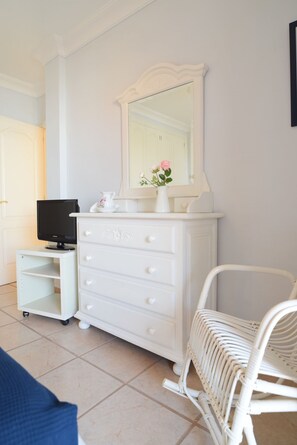 A white dresser with a mirror, a television on a stand, and a wicker chair. - Colonial Suite (Costa Adeje)