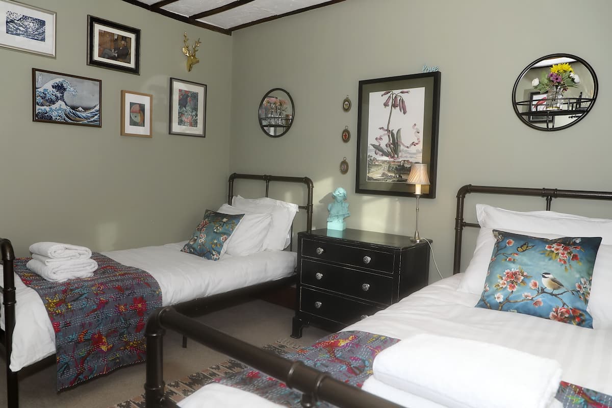A bedroom with two beds, a nightstand, and various framed artworks on the walls.
