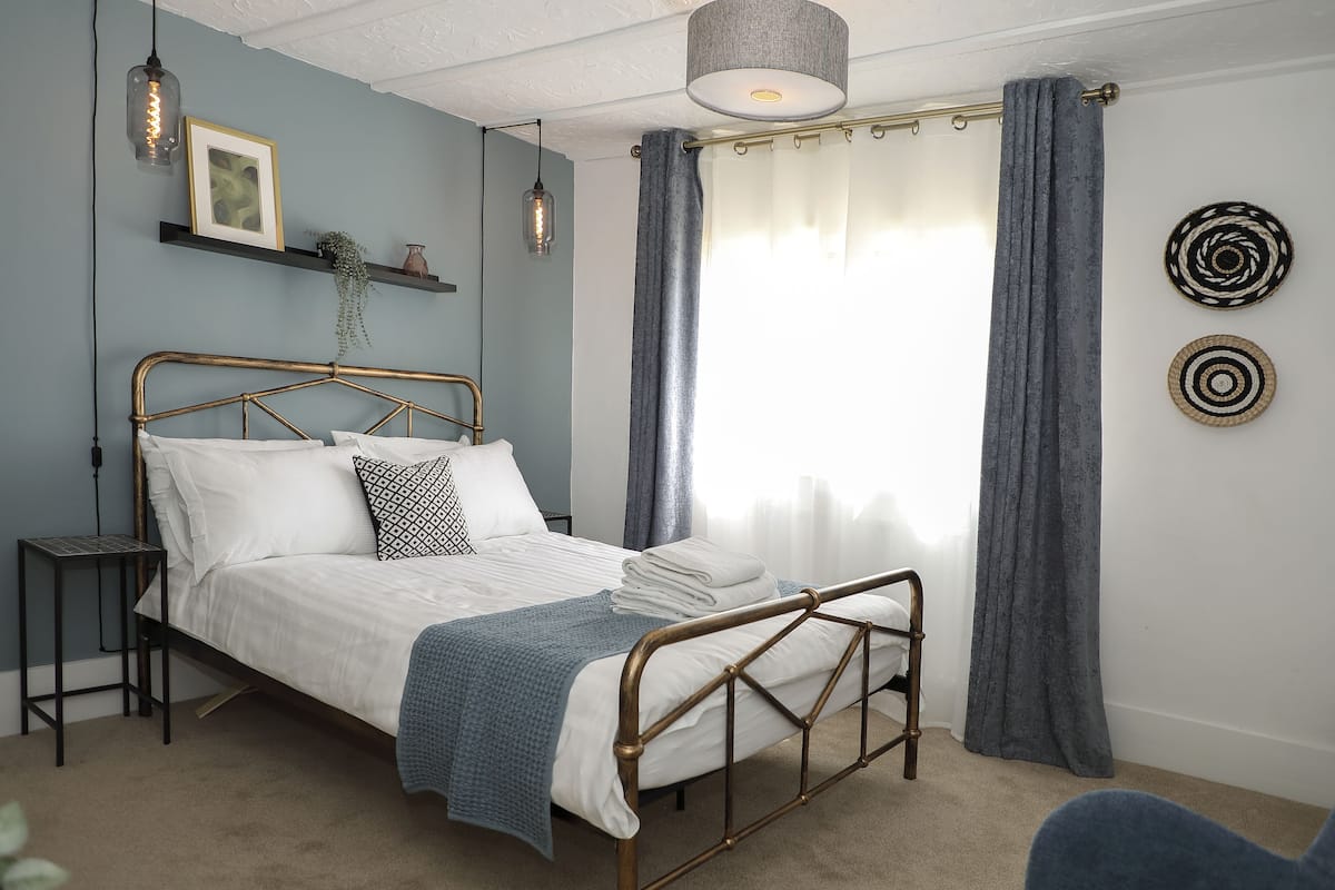 A bedroom with a bed, bedside tables, a hanging light fixture, a window with curtains, and wall decorations.