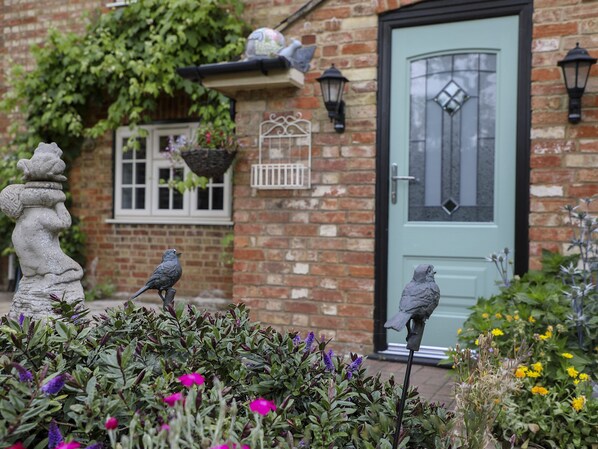 A brick house with a green door, a window with a white frame, and a bird statue in the garden.