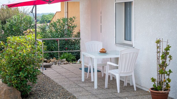 Un patio con una mesa, sillas, una planta en maceta y un paraguas rojo.