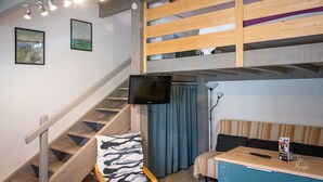 Un interior moderno con una cama litera de madera, una escalera, un televisor de pantalla plana, un sofá y una mesa con un control remoto.