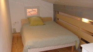 Una cama individual con cabecera de madera y una pequeña ventana encima.