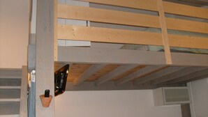 Una cama litera con estructura de madera, una lámpara fijada a la pared y un pequeño estante.