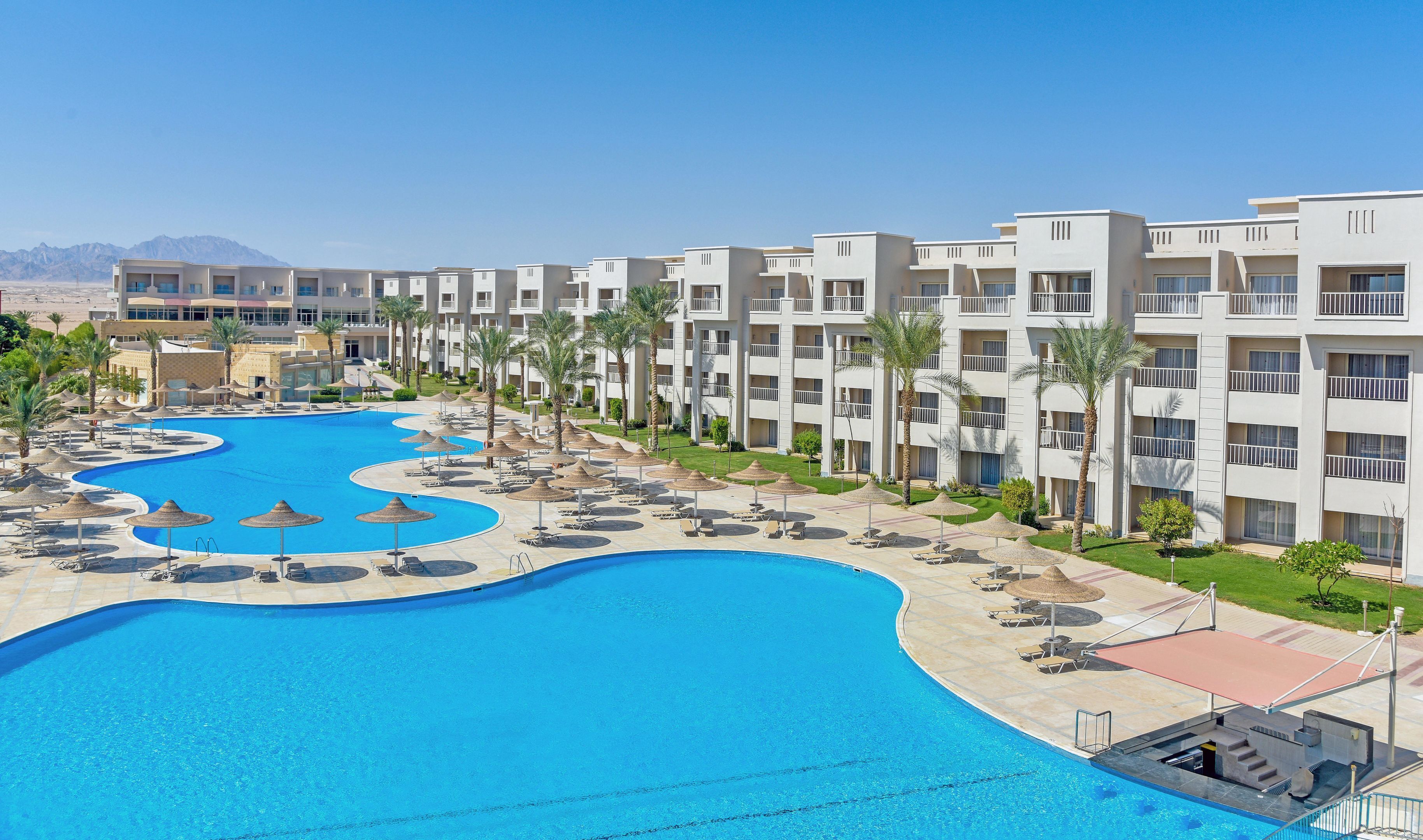 A resort with a large pool, multiple balconies, and palm trees.