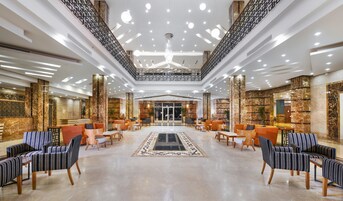Un'ampia hall con una zona salotto centrale, soffitti alti e lampade moderne.