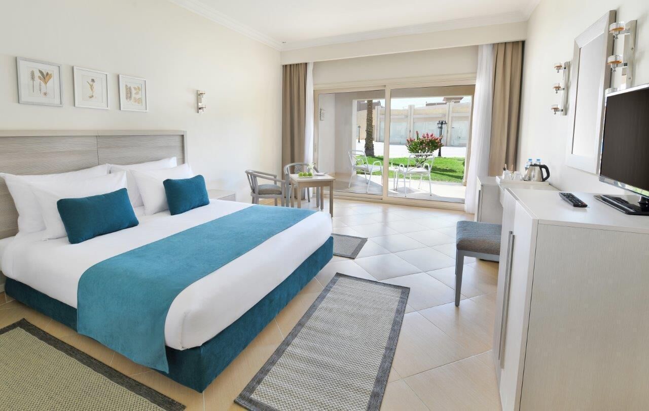 Habitación de hotel con cama, escritorio, silla, televisor y balcón con vistas.