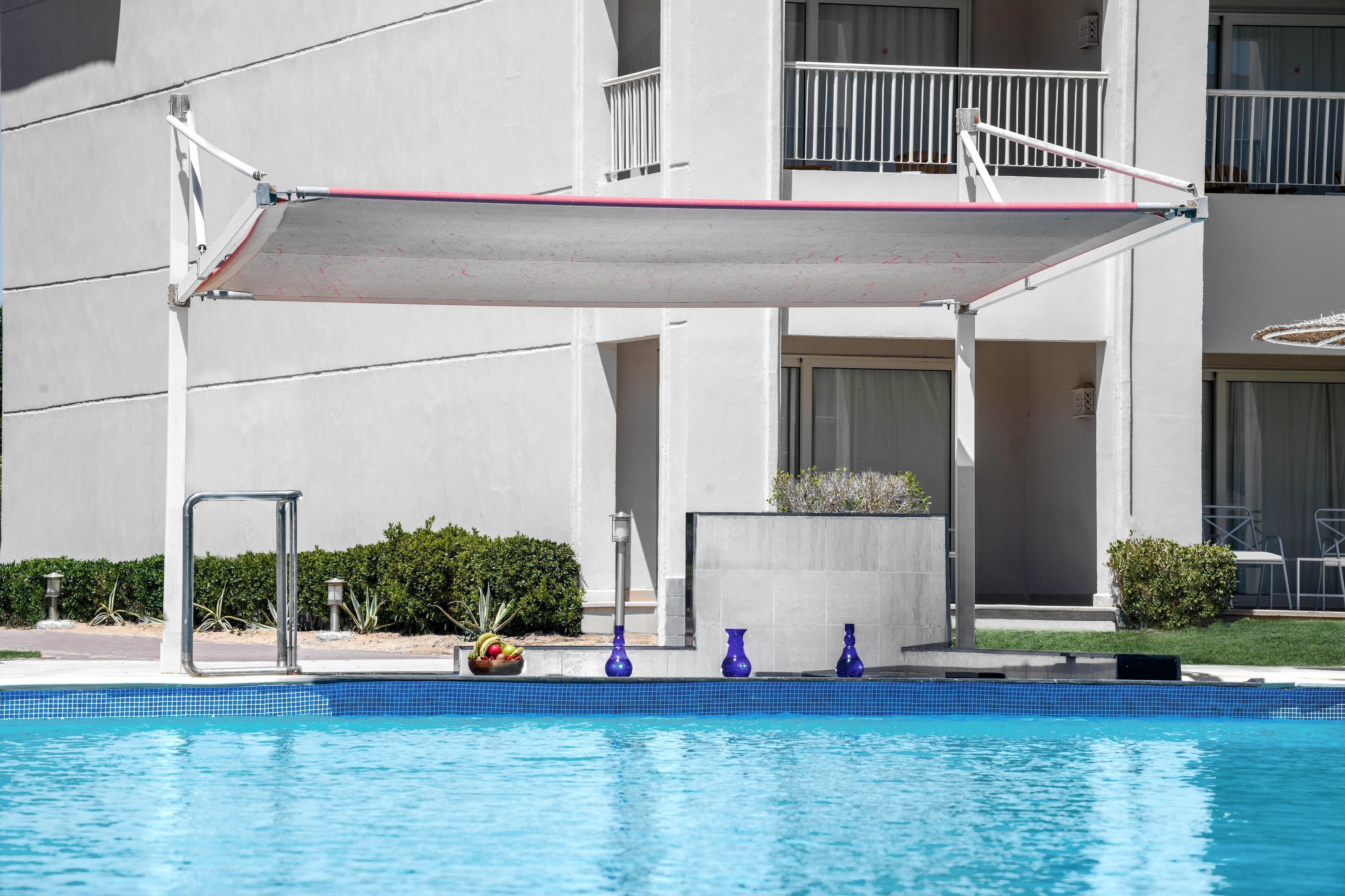 A swimming pool with a sunshade, a metal chair, and a planter with fruit.