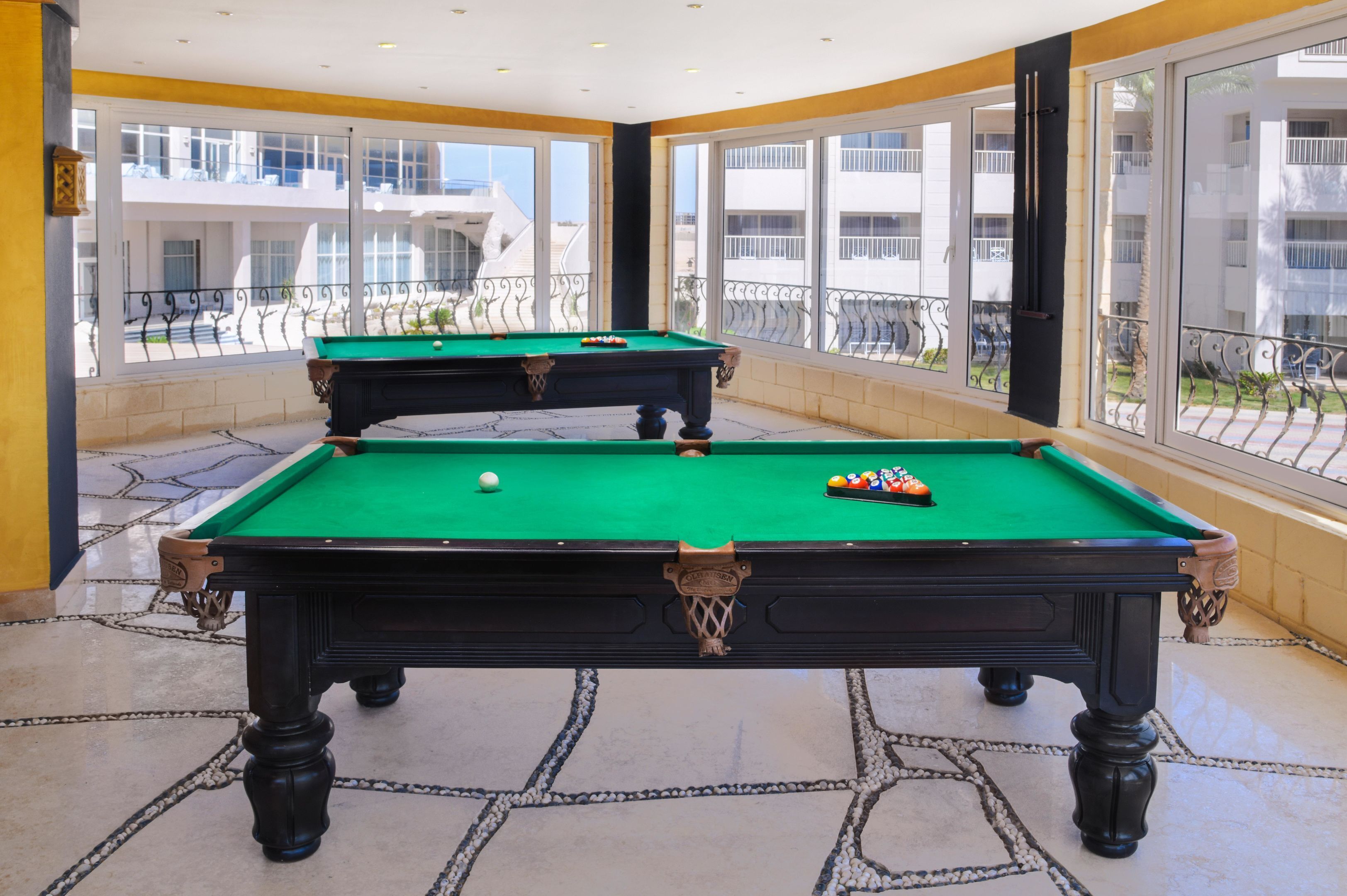 A pool table in a room with large windows and a view of buildings outside.