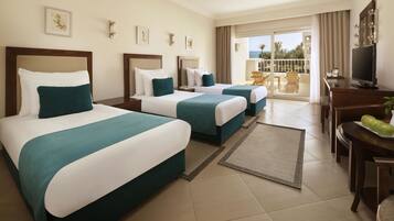 Quarto de hotel com duas camas, uma escrivaninha com televisão e varanda com vista.