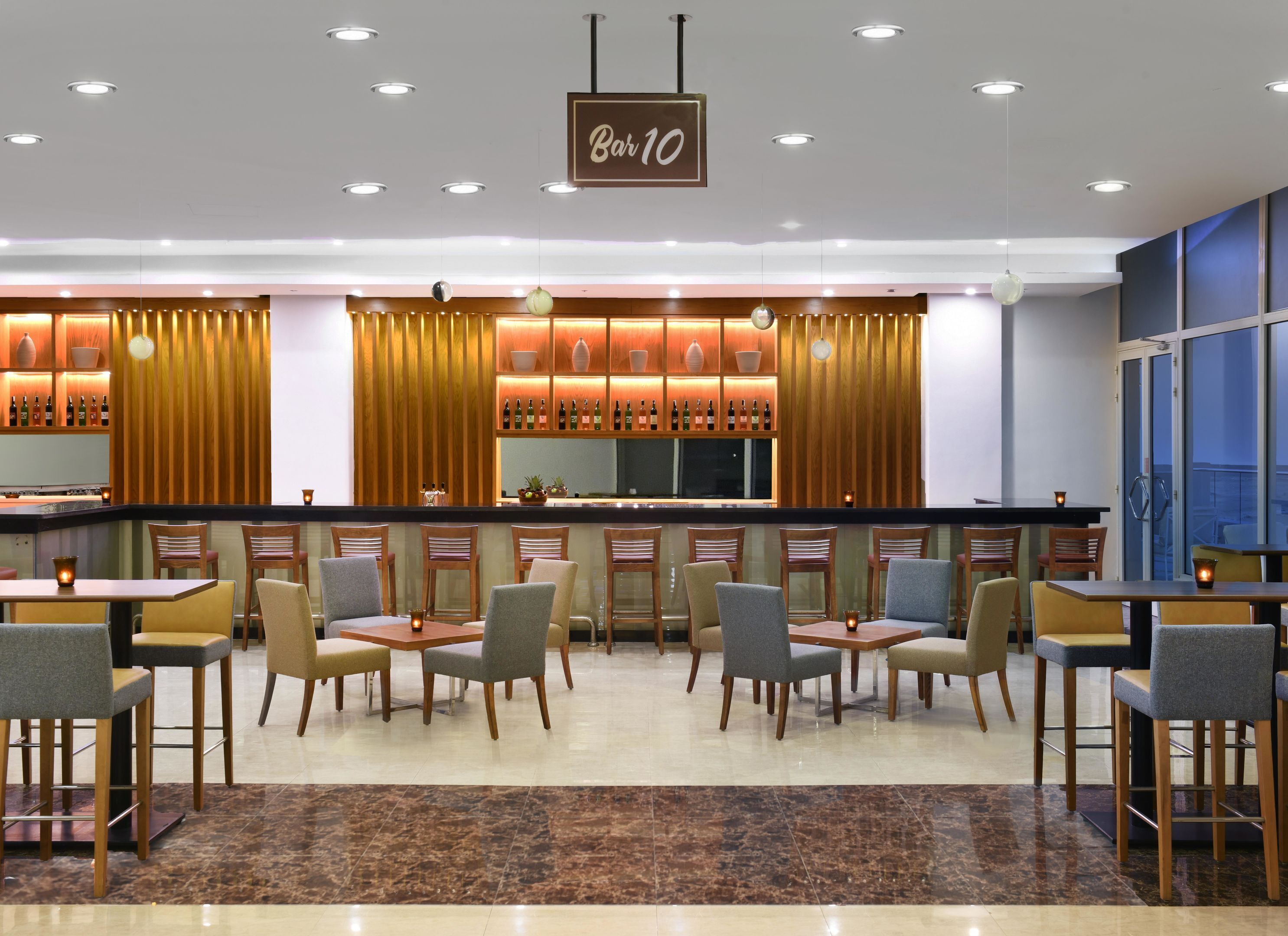 A bar area with a sign reading 'Bar 10,' a seating area with tables and chairs, and a view of the outside through large windows.