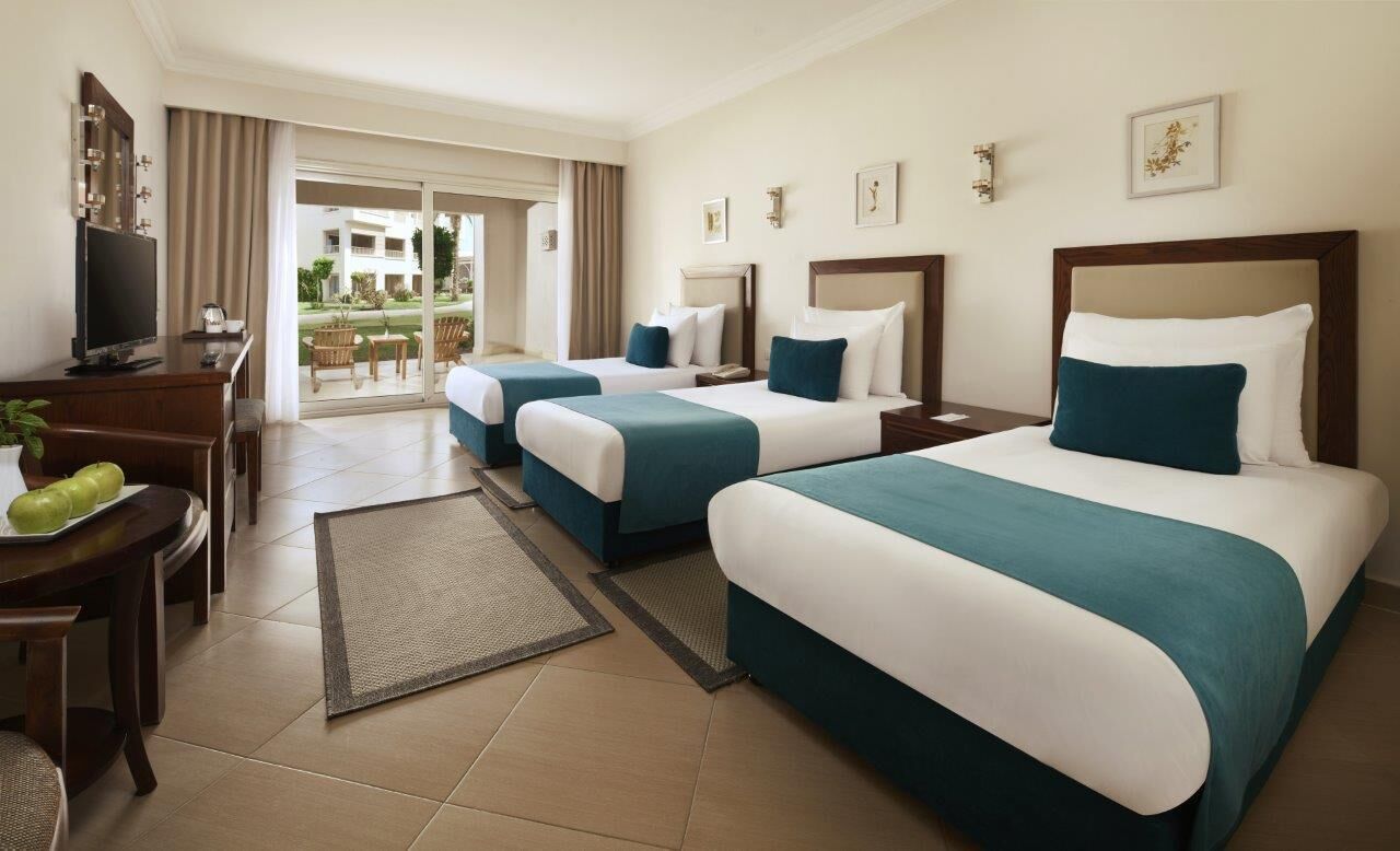 Habitación de hotel con dos camas, un escritorio con televisor y vista al exterior.