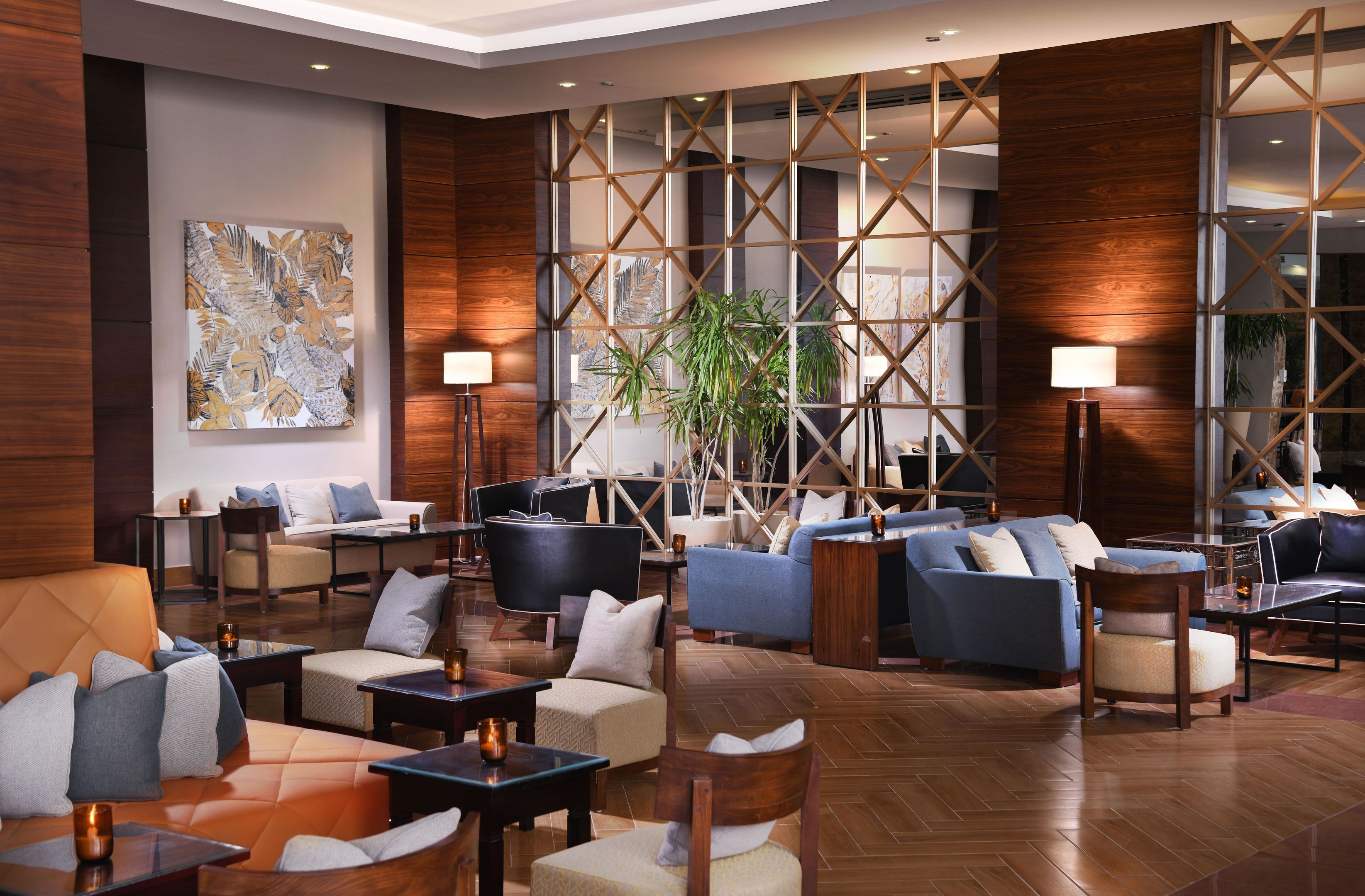 A modern lobby with multiple seating areas, a large abstract painting, and a wooden partition with a geometric design.