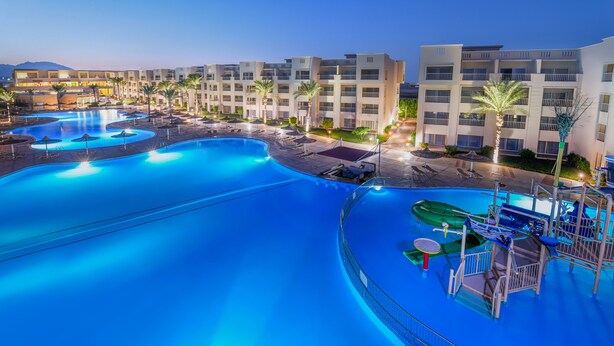 Un complejo turístico con varias piscinas, un parque acuático y una fila de edificios hoteleros.