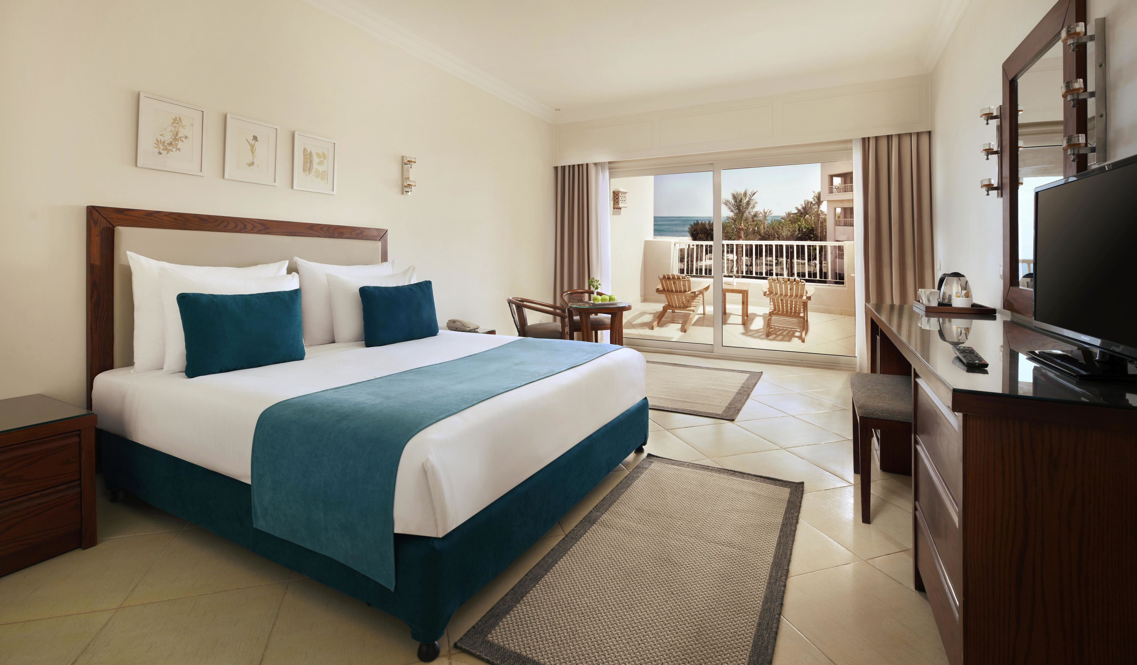 A hotel room with a bed, a TV, a desk, and a balcony with outdoor furniture.