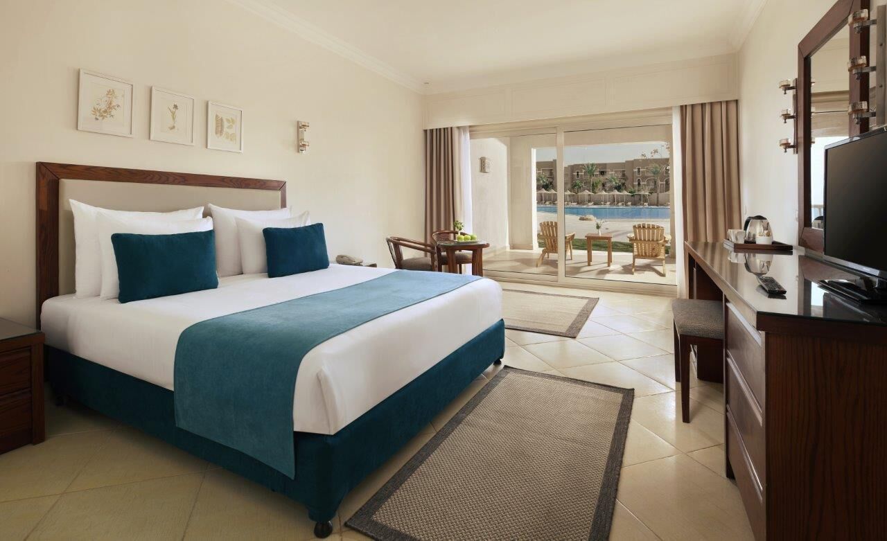 A hotel room with a large bed, a desk, a television, and a view of a pool.