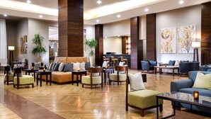 Un vestíbulo amplio con varias zonas de estar, incluyendo sofás y sillones, y un mostrador de recepción al fondo.