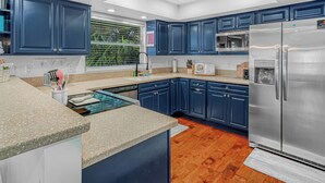 A modern kitchen with dark blue cabinets, a stainless steel refrigerator, and a window with greenery outside. - Modern Waterfront Lakehouse, with a private beach and a spacious boat dock. (Lake Placid)