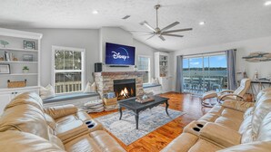 A living room with a fireplace, leather sofa, and a television displaying 'Disney+'. - Modern Waterfront Lakehouse, with a private beach and a spacious boat dock. (Lake Placid)
