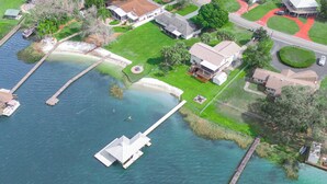 An aerial view of a residential area with a dock extending into a body of water, surrounded by houses and greenery. - Modern Waterfront Lakehouse, with a private beach and a spacious boat dock. (Lake Placid)