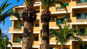 Un hotel de varios pisos con balcones, palmeras y un cielo azul despejado.
