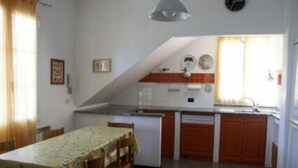 Una cuina compacta amb zona de menjador, que inclou una taula amb caires, un refrigerador, un rentaplat i un rellotge a la paret.