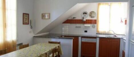 Cozinha compacta com área de jantar, apresentando uma mesa com cadeiras, geladeira, pia e um relógio na parede.