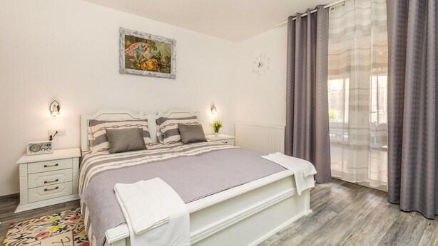 Ein Schlafzimmer mit einem Bett, Nachttischen, einem Radio, einem Bild und einem Fenster mit Vorhängen.