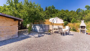Eine Holzhütte mit Whirlpool, Grill und Tisch mit Stühlen unter einem Sonnenschirm.