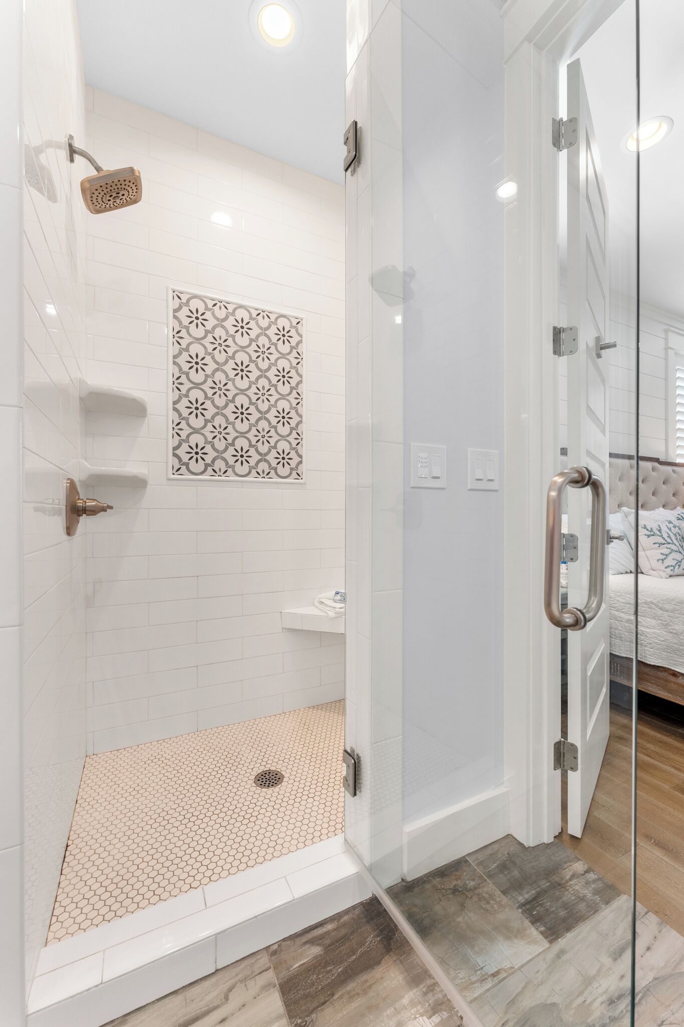 Un baño moderno con cabina de ducha de vidrio, paredes de azulejos blancos y suelo de baldosas estampadas.