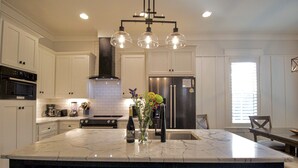 Una cocina moderna con armarios blancos, una isla grande con encimera de mármol, un refrigerador de acero inoxidable y una campana extractora negra.