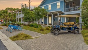 Una casa de dos pisos con un porche, un carrito de golf y bicicletas estacionadas afuera.