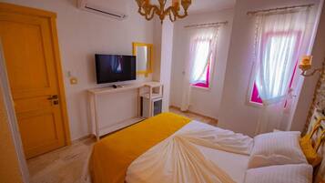 A hotel room with a bed, a TV, a desk, and a window with curtains.