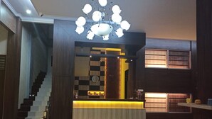 Un hall d’hôtel moderne avec un comptoir d’accueil, un lustre, un escalier et une vue sur l’intérieur.
