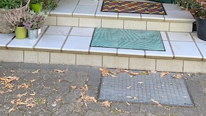 Una porta verde a due ante con un piccolo oblò, una cassetta delle lettere e una casetta per uccelli a sinistra.