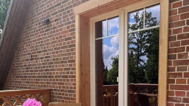 Un patio in legno con tavolo e sedie, una porta vetrata che dà sull'esterno e un muro in mattoni.