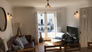 Ett vardagsrum med en soffa, en tv, ett matbord med apelsiner och en balkong med utsikt.