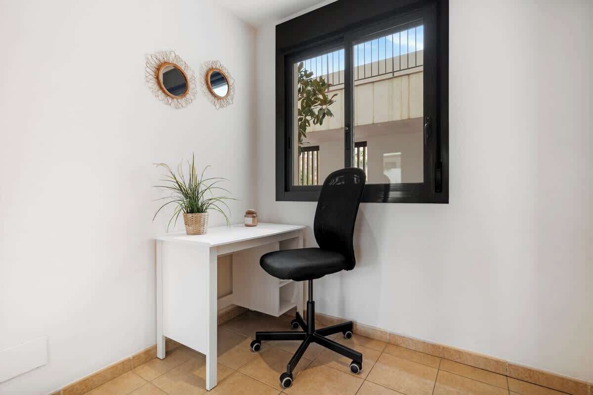 Un petit bureau avec un bureau blanc, une chaise de bureau noire, une plante en pot et deux miroirs décoratifs accrochés au mur.