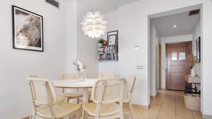 A dining area with a round table and six wicker chairs, a pendant light, a framed picture on the wall, and a bookshelf with books and a plant. - Alamar apt in Mijas by Costarentals - Ref 38 (Las Lagunas de Mijas)