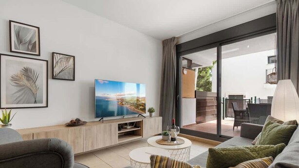 A modern living room with a flat-screen TV, a sofa, a coffee table, and a sliding glass door leading to an outdoor area. - Alamar apt in Mijas by Costarentals - Ref 38 (Las Lagunas de Mijas)