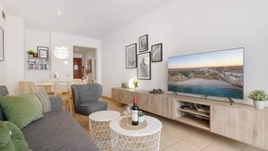 A modern living room with a large flat-screen TV, a grey sofa, two white round side tables, and a wooden entertainment unit. - Alamar apt in Mijas by Costarentals - Ref 38 (Las Lagunas de Mijas)