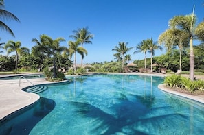 A clear blue swimming pool surrounded by palm trees and greenery.