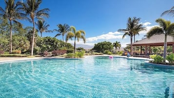 Relax by the resort pool surrounded by lush greenery and palm trees.