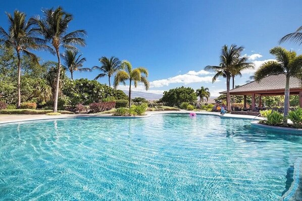 Relax by the resort pool surrounded by lush greenery and palm trees.