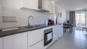 A modern kitchen with white cabinets, a stainless steel sink, and a built-in oven. There is a dining area with a table and chairs, and a view of a balcony with a railing. - Central apartment with balcony by Costarentals - Ref 92 (Costa del Sol)