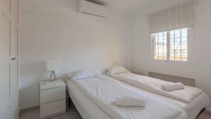 A bedroom with two beds, a nightstand, a lamp, a window with a view, and an air conditioning unit. - Central apartment with balcony by Costarentals - Ref 92 (Costa del Sol)