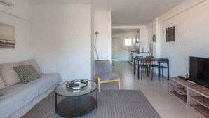 A modern living room with a sofa, coffee table, and TV stand. There is a dining area with a table and chairs. - Central apartment with balcony by Costarentals - Ref 92 (Costa del Sol)