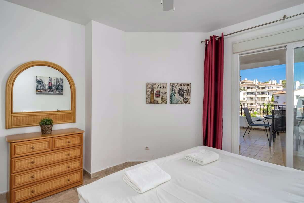Une chambre à coucher avec un lit, une commode, un miroir et une vue sur l’extérieur.